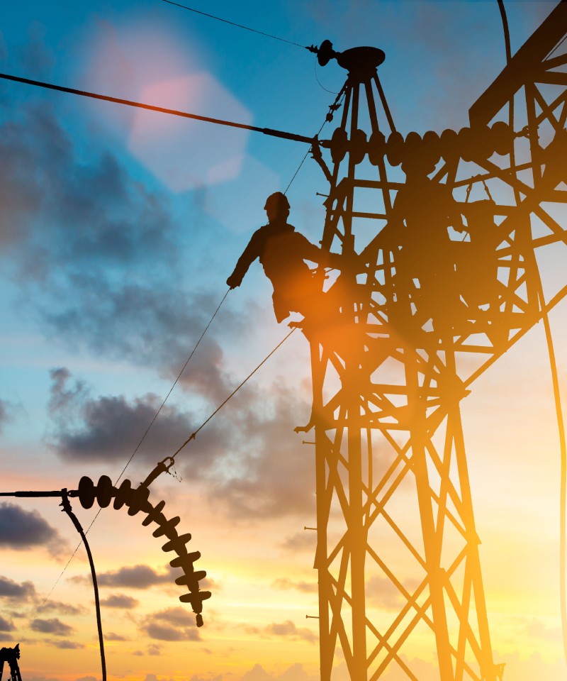 Worker on an electric pylon in the sunset