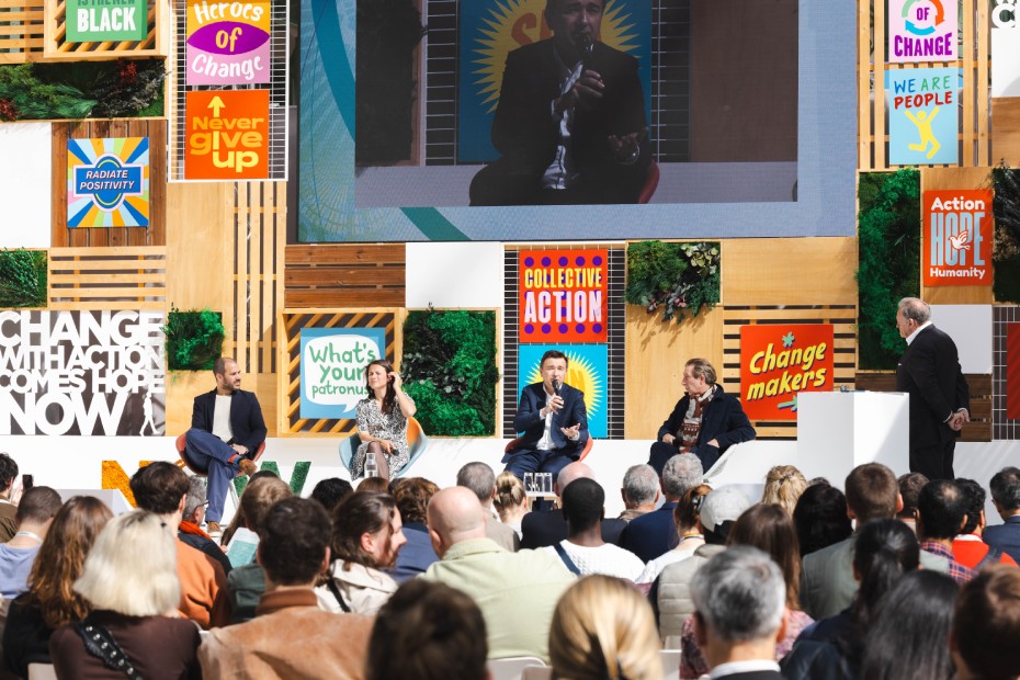 Conference at the ChangeNOW event, with four speakers discussing on stage in front of an audience, surrounded by colorful panels bearing inspirational messages.
