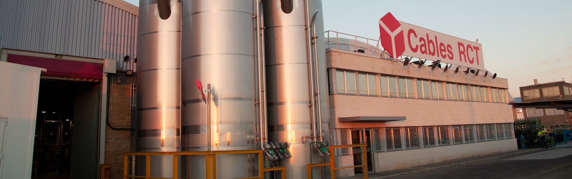 Exterior view of a modern industrial building with stainless steel silos and a large sign.