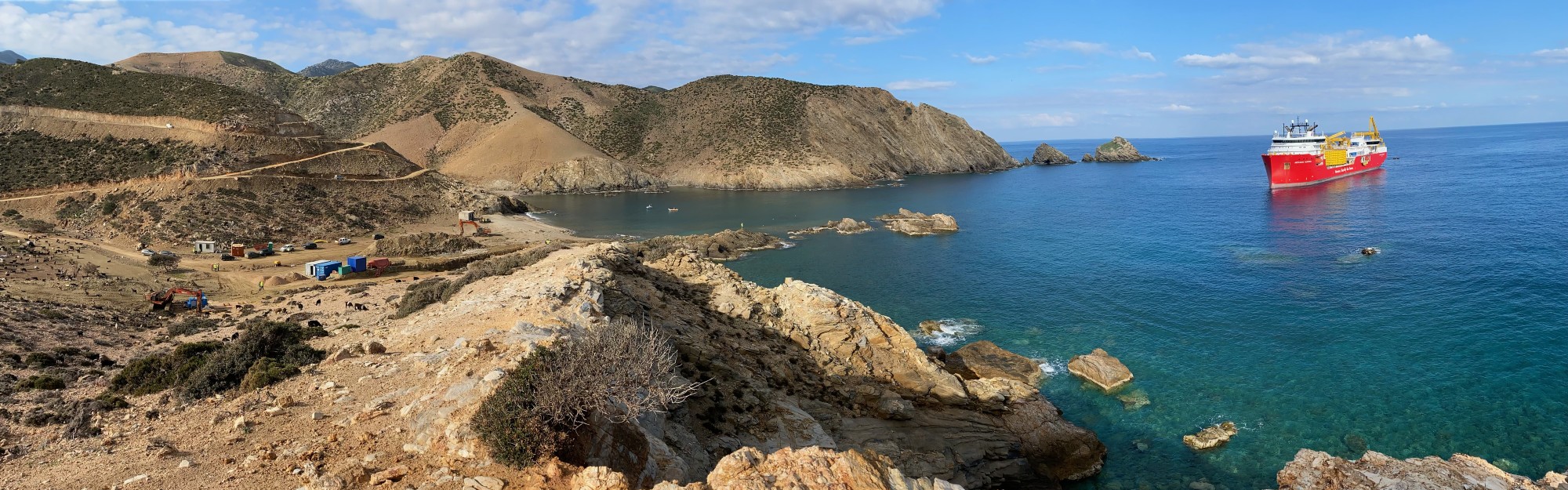 Scenic coastal view with rocky terrain and large ship in clear blue waters