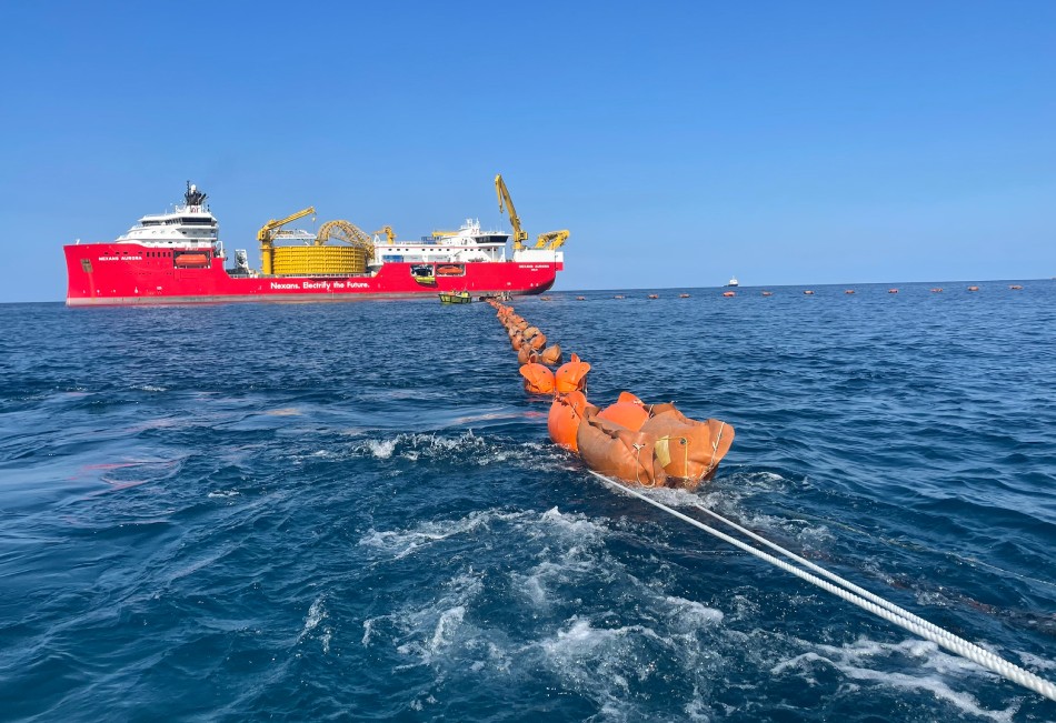 A large red ship at sea with a long cable and orange buoys in the water.