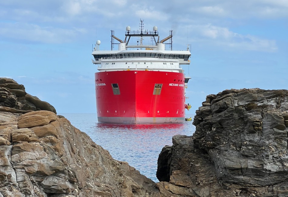 Red ship in calm waters surrounded by rocky coastline under a blue sky.