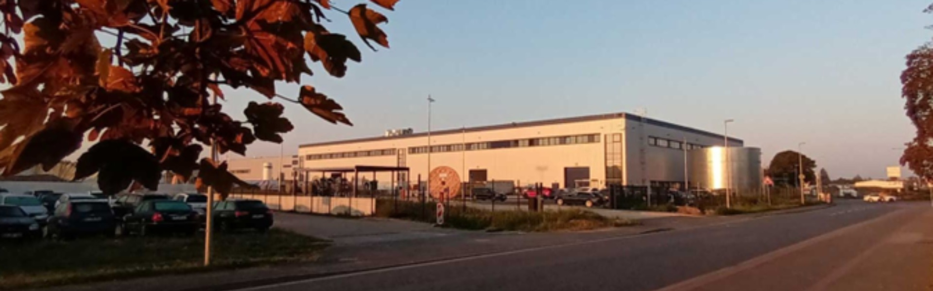 Industrial building with vehicles parked outside, illuminated by sunset.