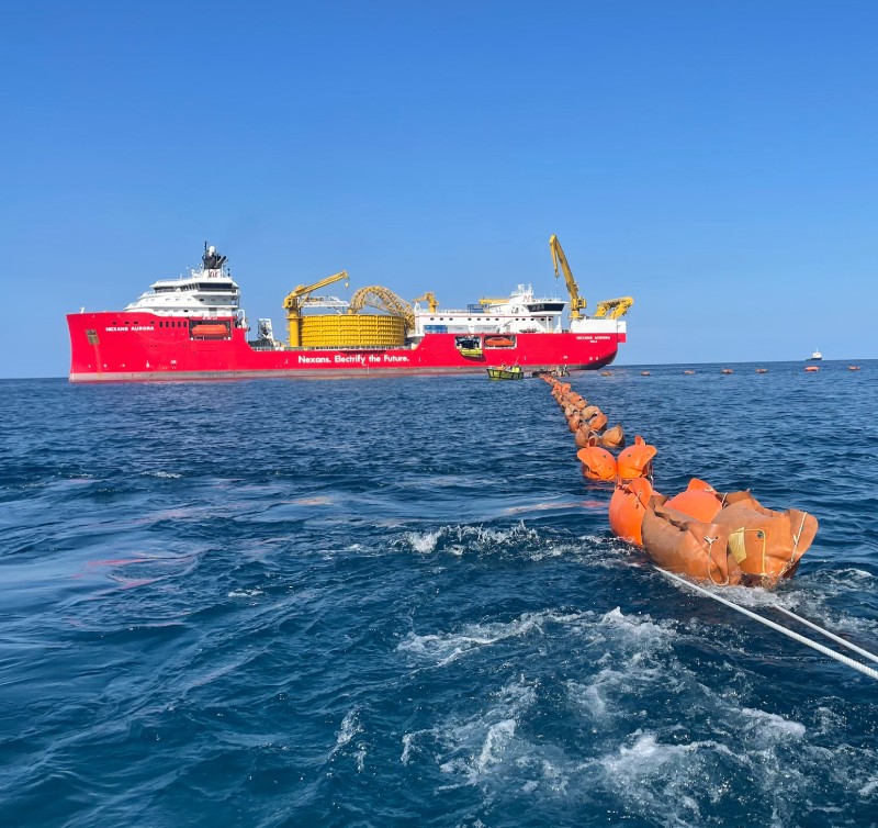Red cable-laying ship at sea with a long cable trailing behind it.