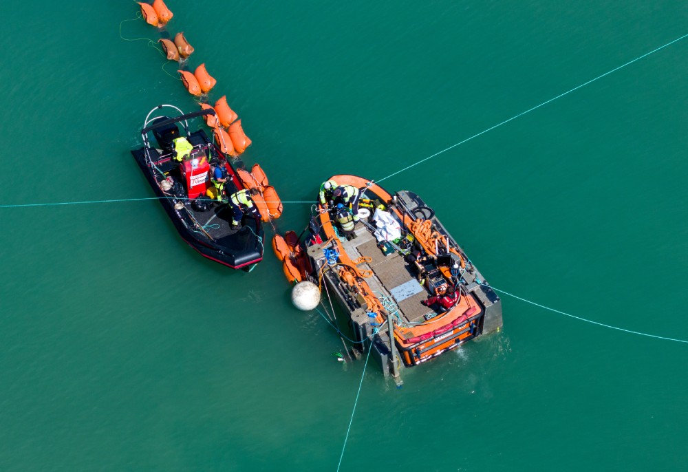 Two boats engaged in marine operations, with orange buoyancy aids visible on the water.