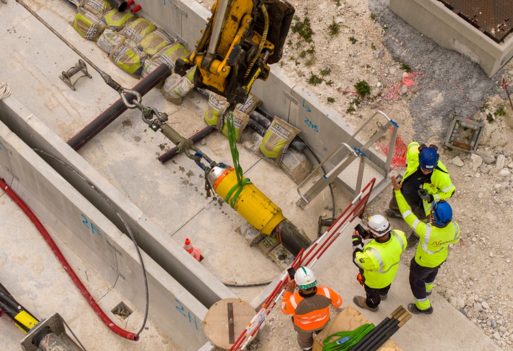Civil engineering site with workers overseeing equipment and materials in a trench.