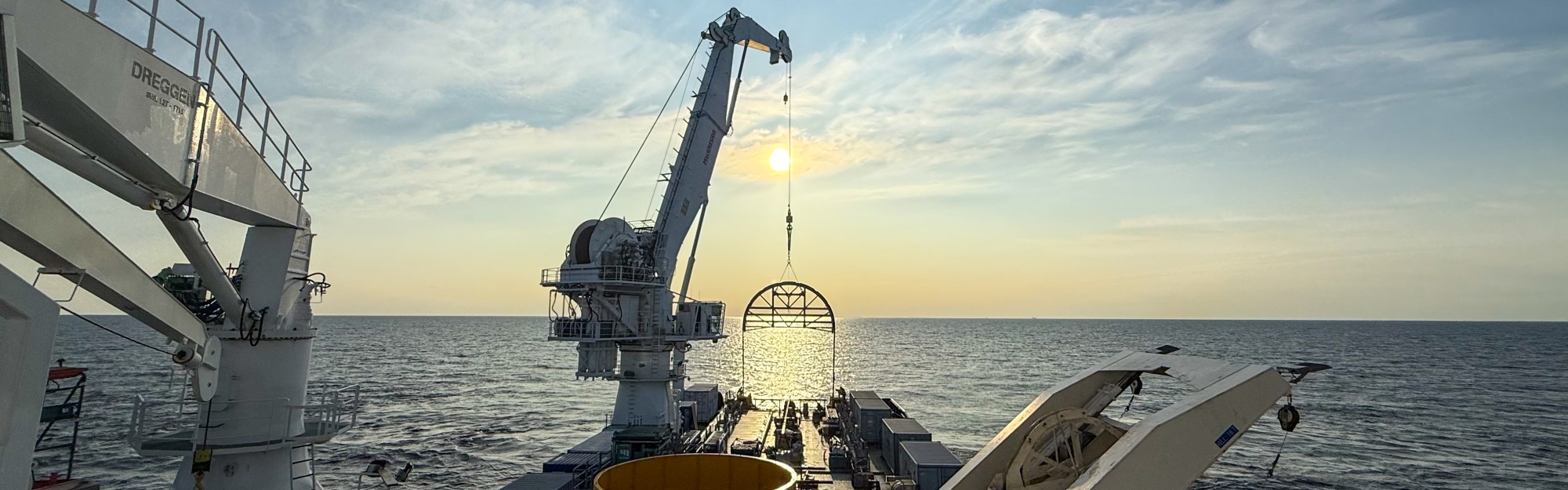Grue d'un navire en mer soulevant un équipement au coucher du soleil
