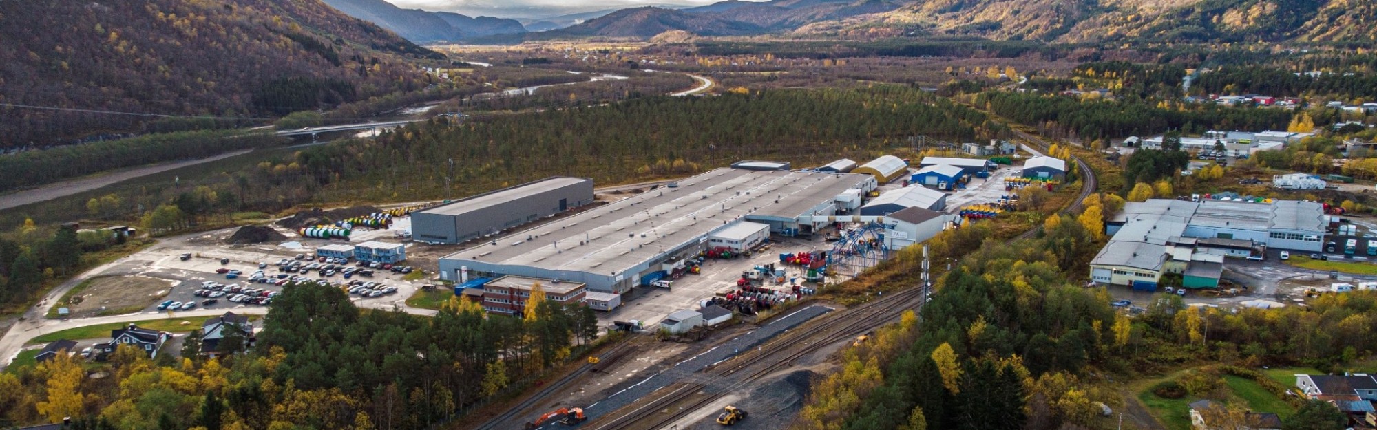 Aerial view of a large industrial facility surrounded by autumn foliage and mountains.
