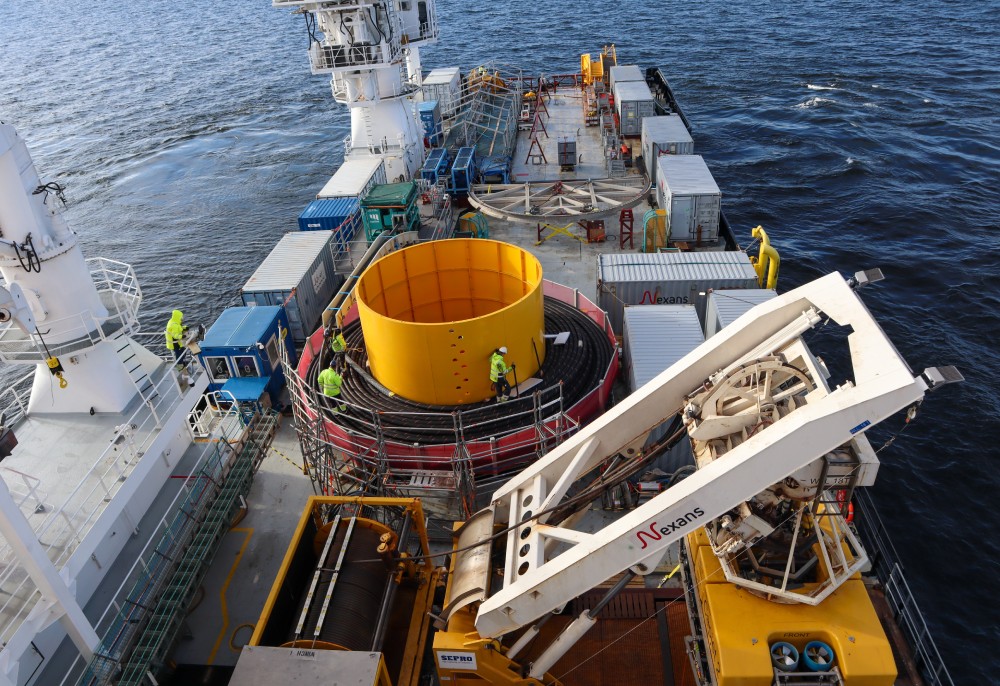 View of a marine operation with workers and large yellow equipment on a ship deck.