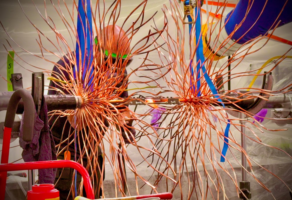 Copper wires resembling a starburst shape, with a technician working in the background.