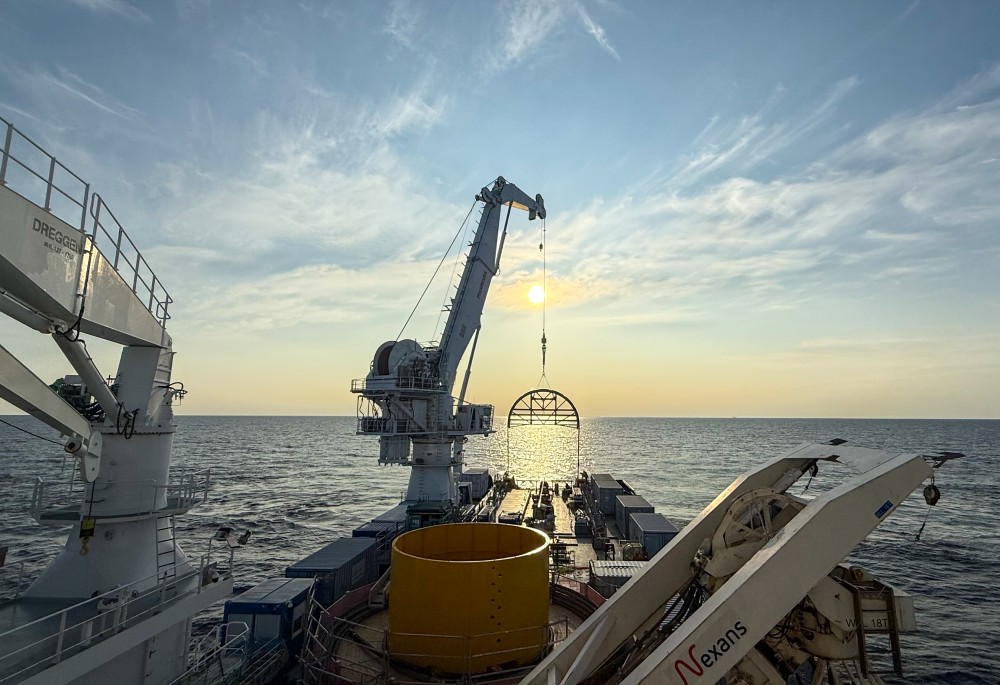 Ship deck with a crane lifting equipment over the ocean at sunset.