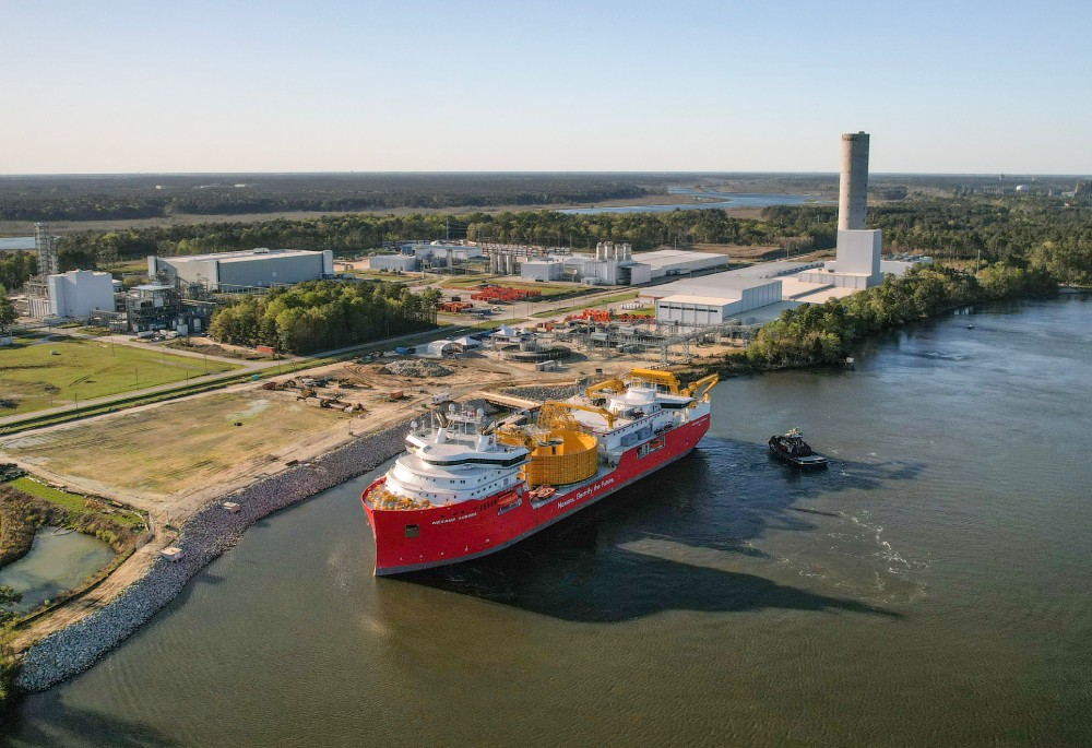 Aerial view of a red offshore support vessel near an industrial site and a river