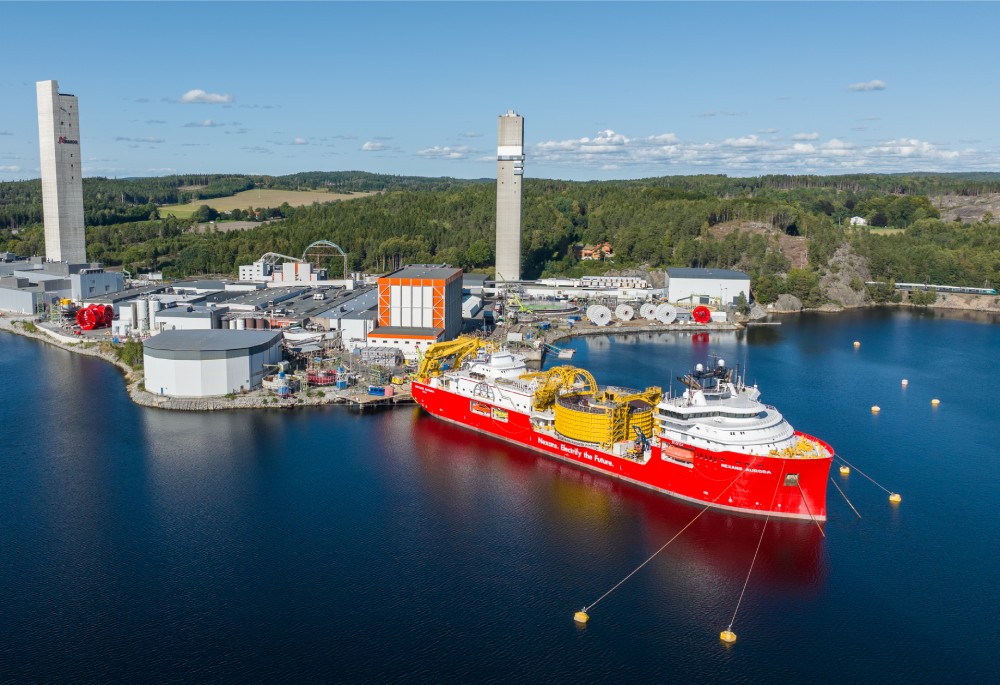 Aerial view of a large red construction vessel docked at an industrial site near calm waters.