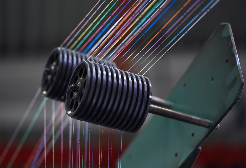 Close-up of a machine with colorful threads and wheels, showcasing intricate engineering and design.