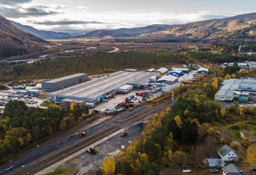 Aerial view of a large industrial complex surrounded by mountains and greenery.